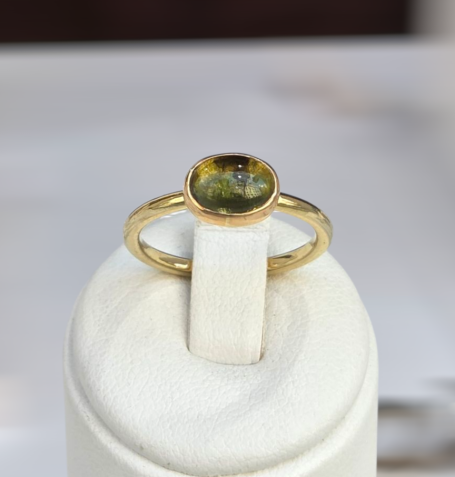 Goldring mit ovalem, grünem Edelstein auf einem weißen Sockel.